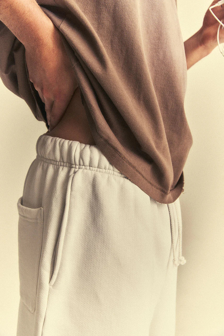 Person wearing a brown shirt and beige pants against a neutral background