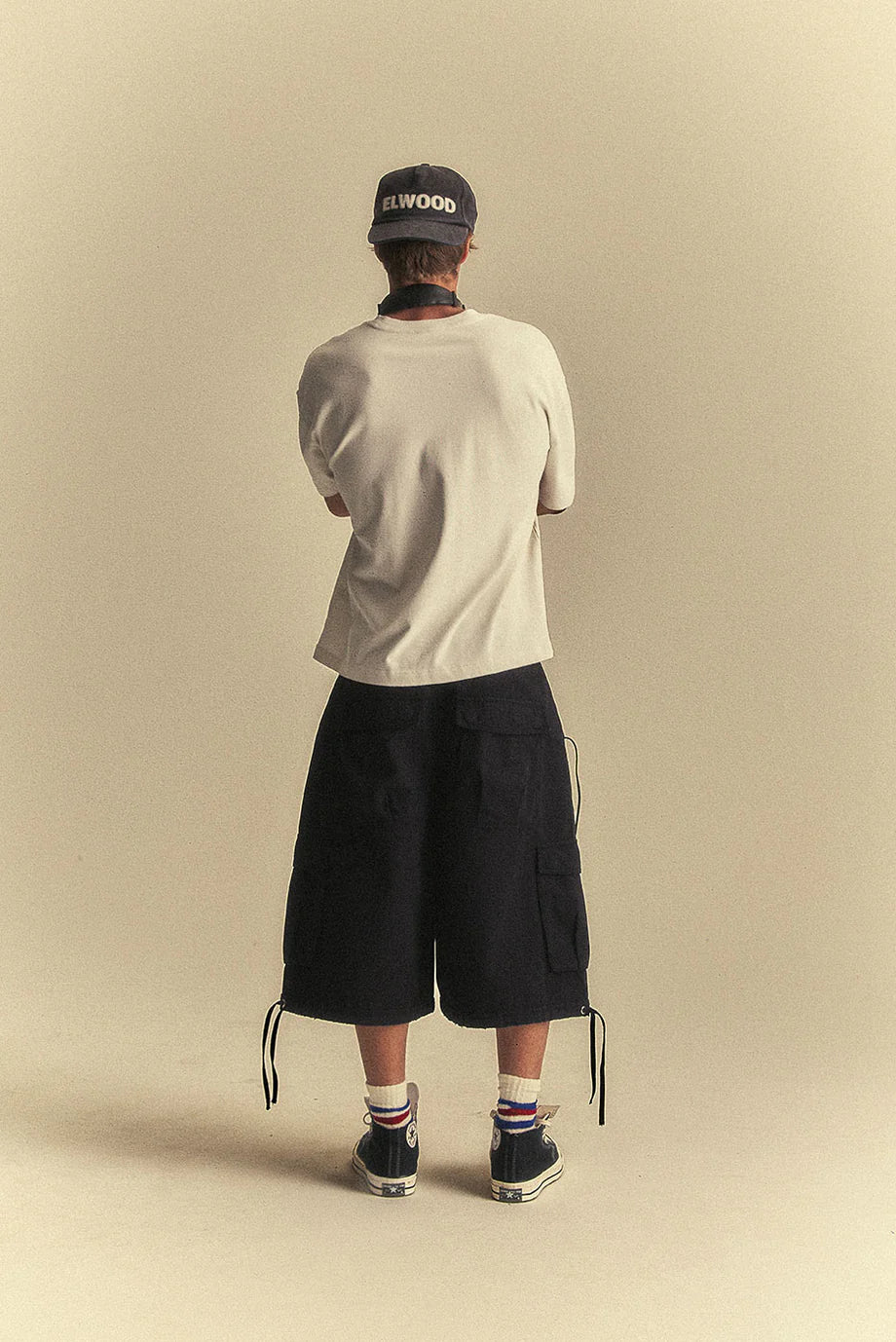 Person wearing a beige t-shirt, black shorts, and a cap on a beige background