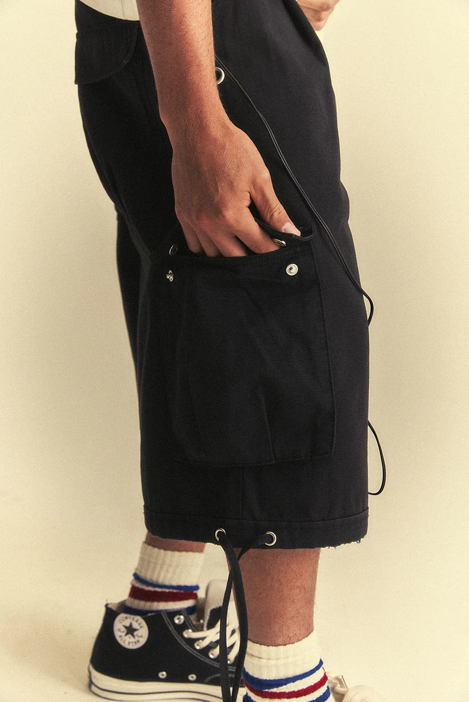 Person wearing black shorts and Converse shoes on a beige background