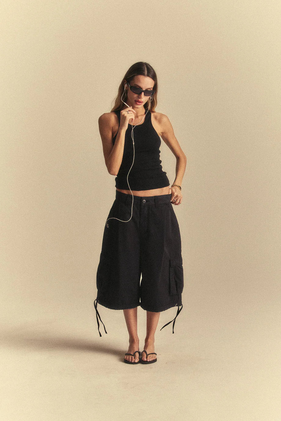 Woman wearing a black sleeveless top and black cargo shorts on a beige background