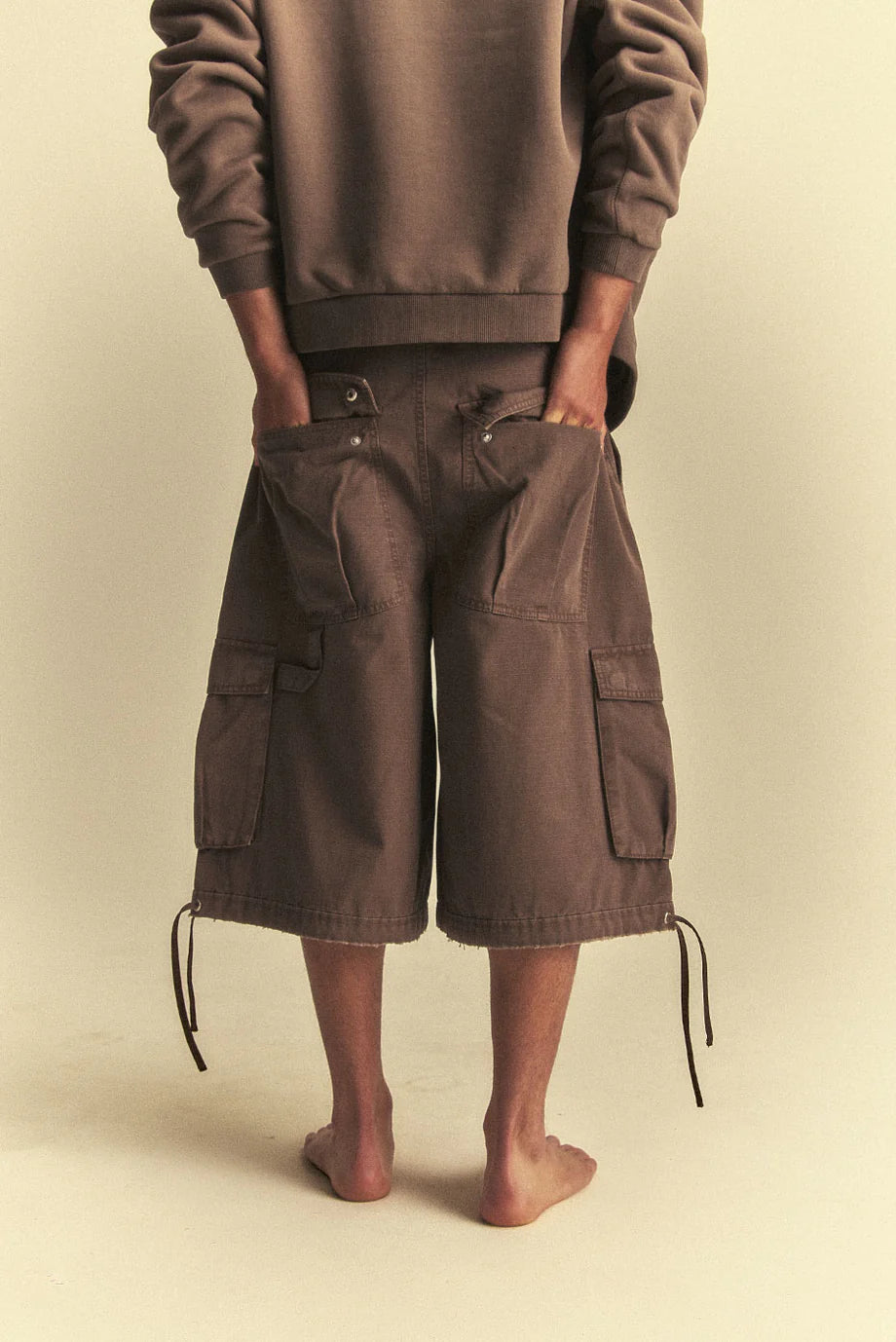 Person wearing a brown outfit with cargo shorts on a beige background