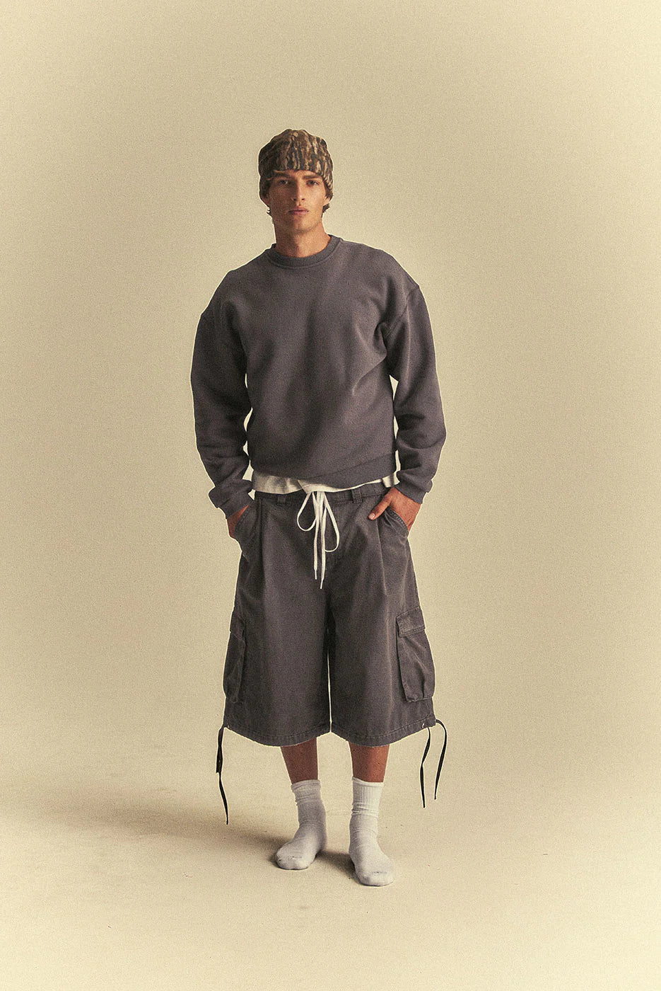 Person wearing a grey sweatshirt and cargo shorts on a beige background