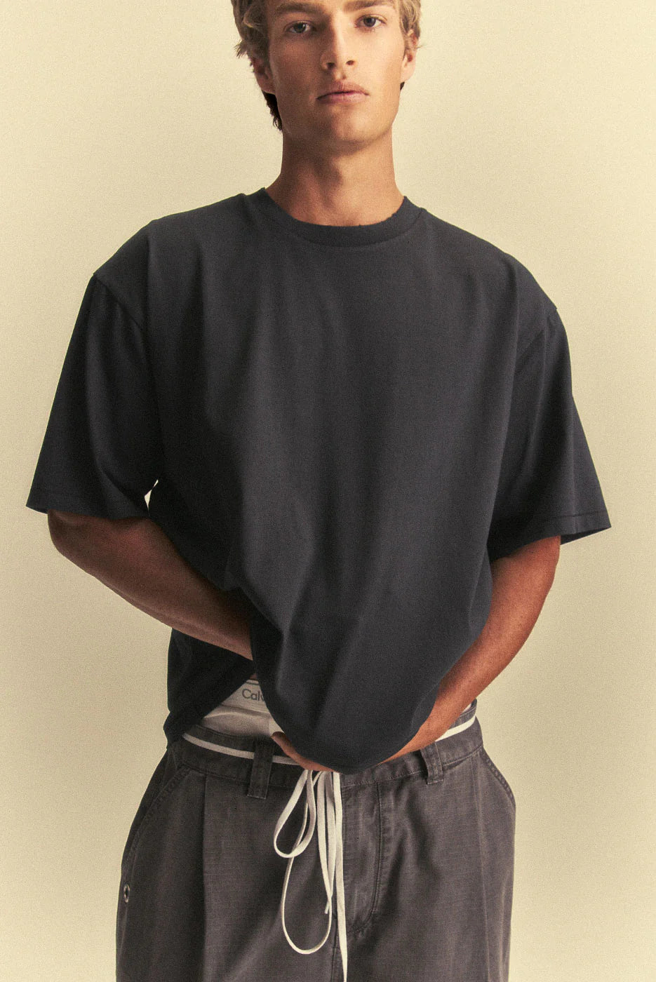 Person wearing a black oversized t-shirt and dark pants against a beige background