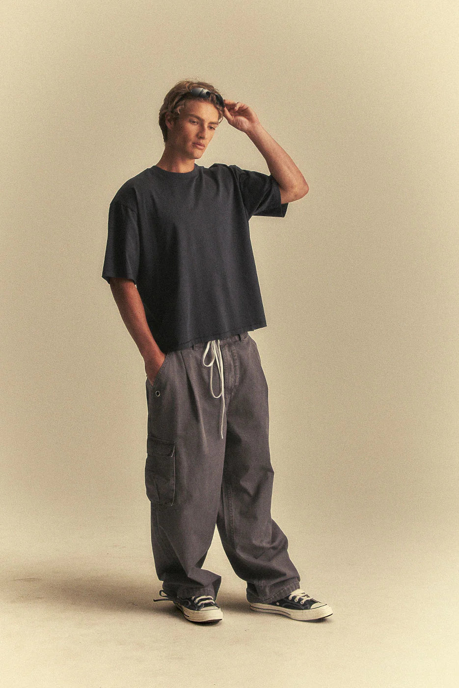 Person wearing a black t-shirt and grey pants on a beige background