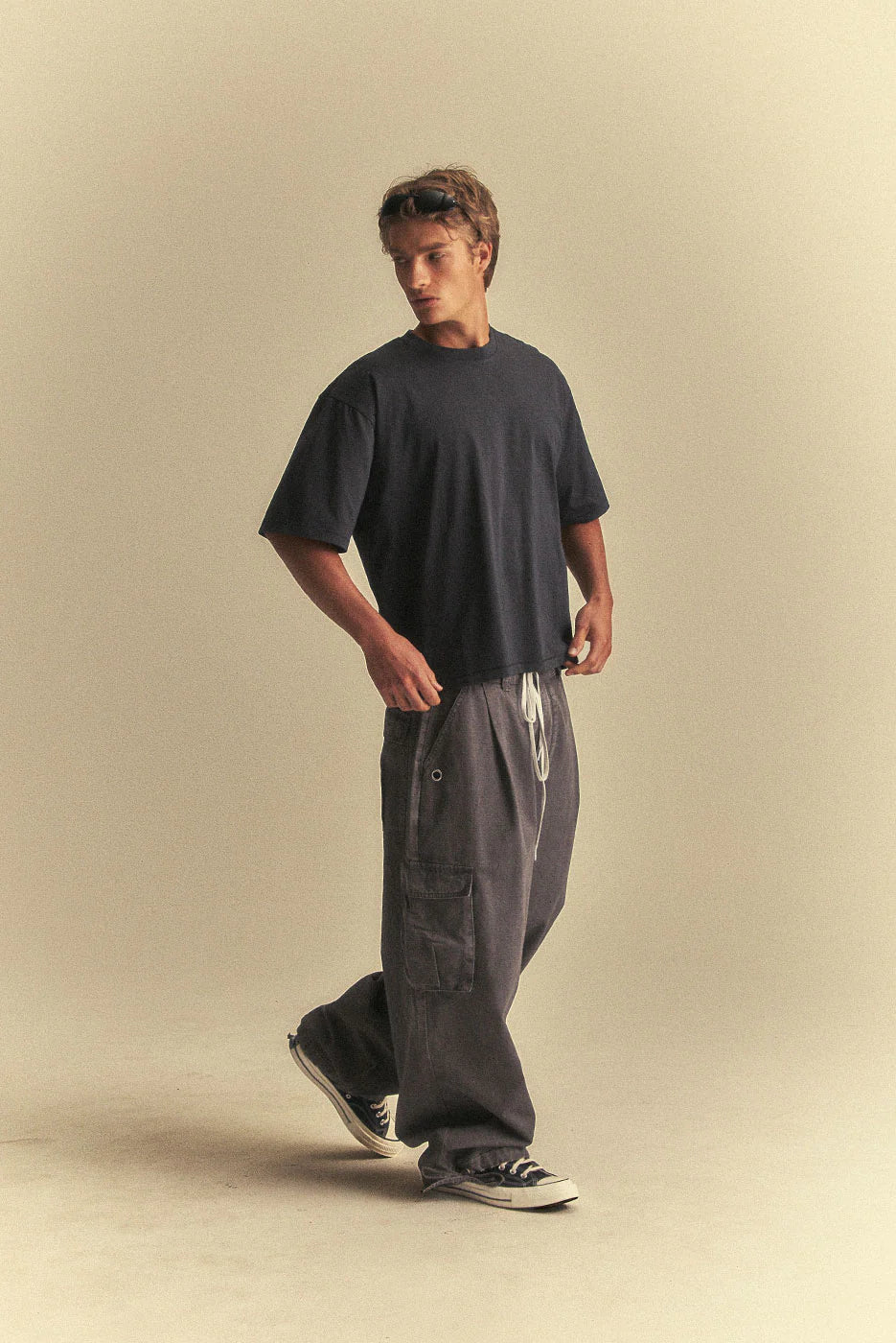 Man wearing a black t-shirt and grey cargo pants on a beige background