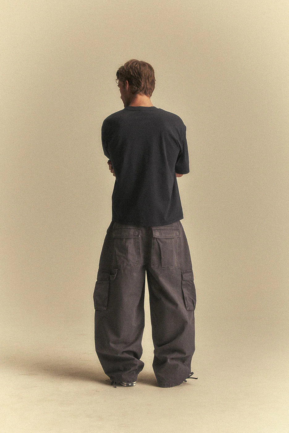 Person wearing a black shirt and dark grey cargo pants on a beige background