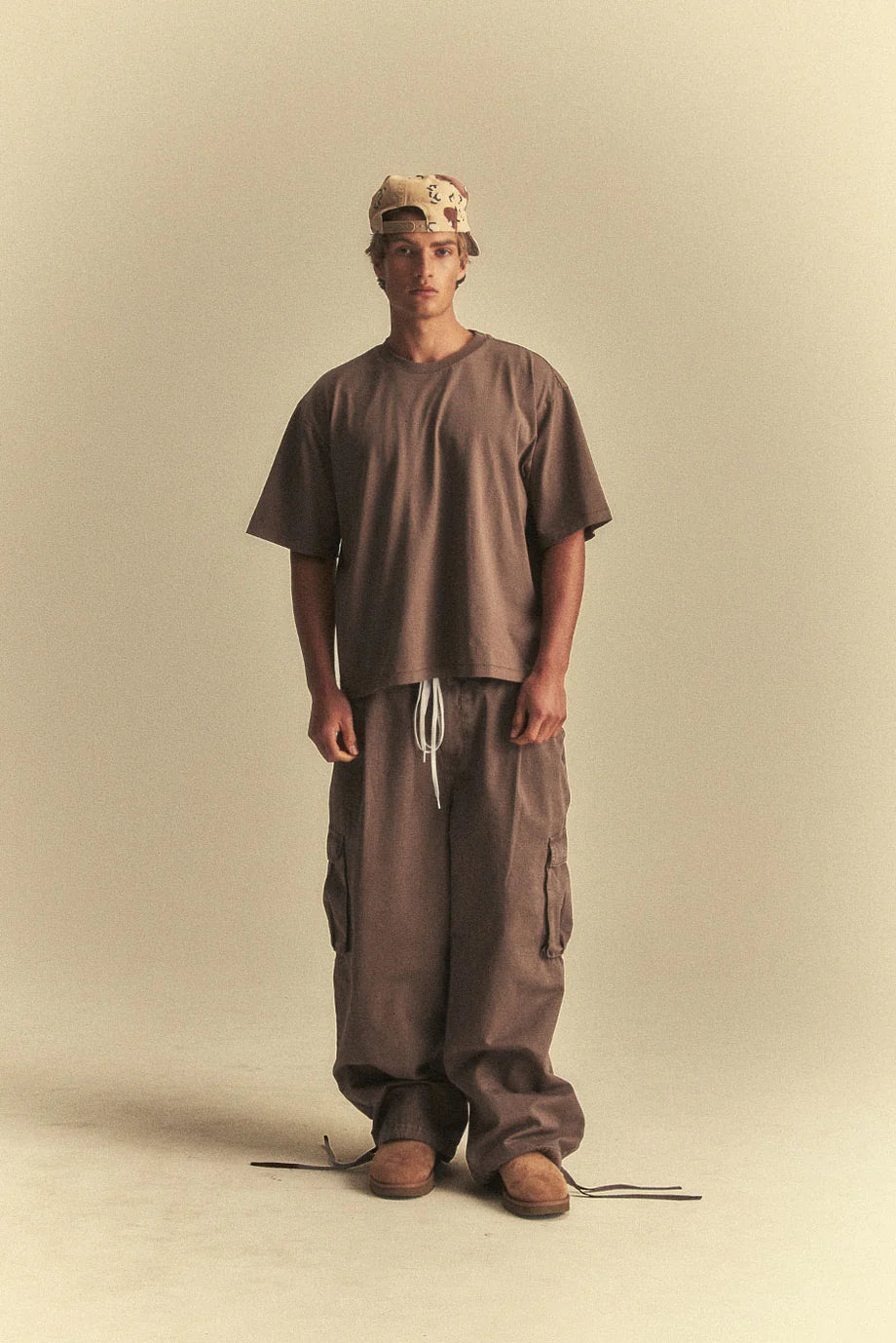 Person wearing a brown outfit with a cap on a beige background