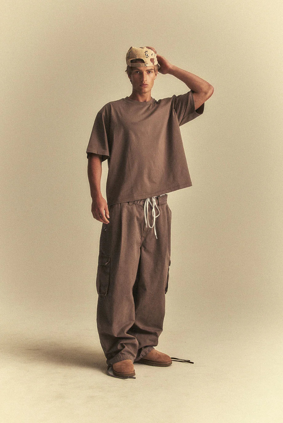 Person wearing a brown outfit with a cap on a beige background