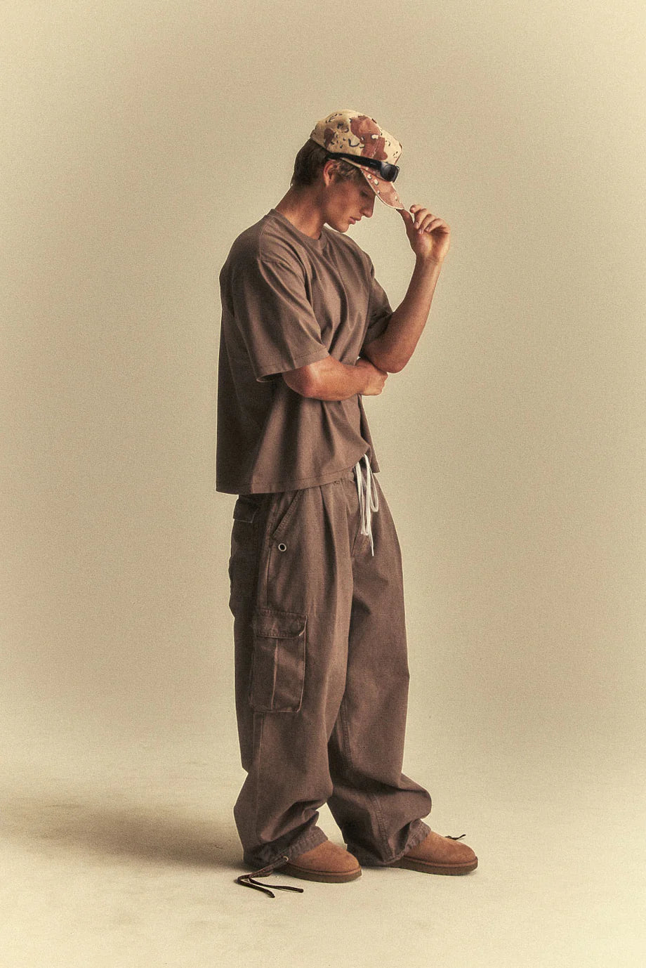 Person wearing a brown outfit and cap, standing against a beige background