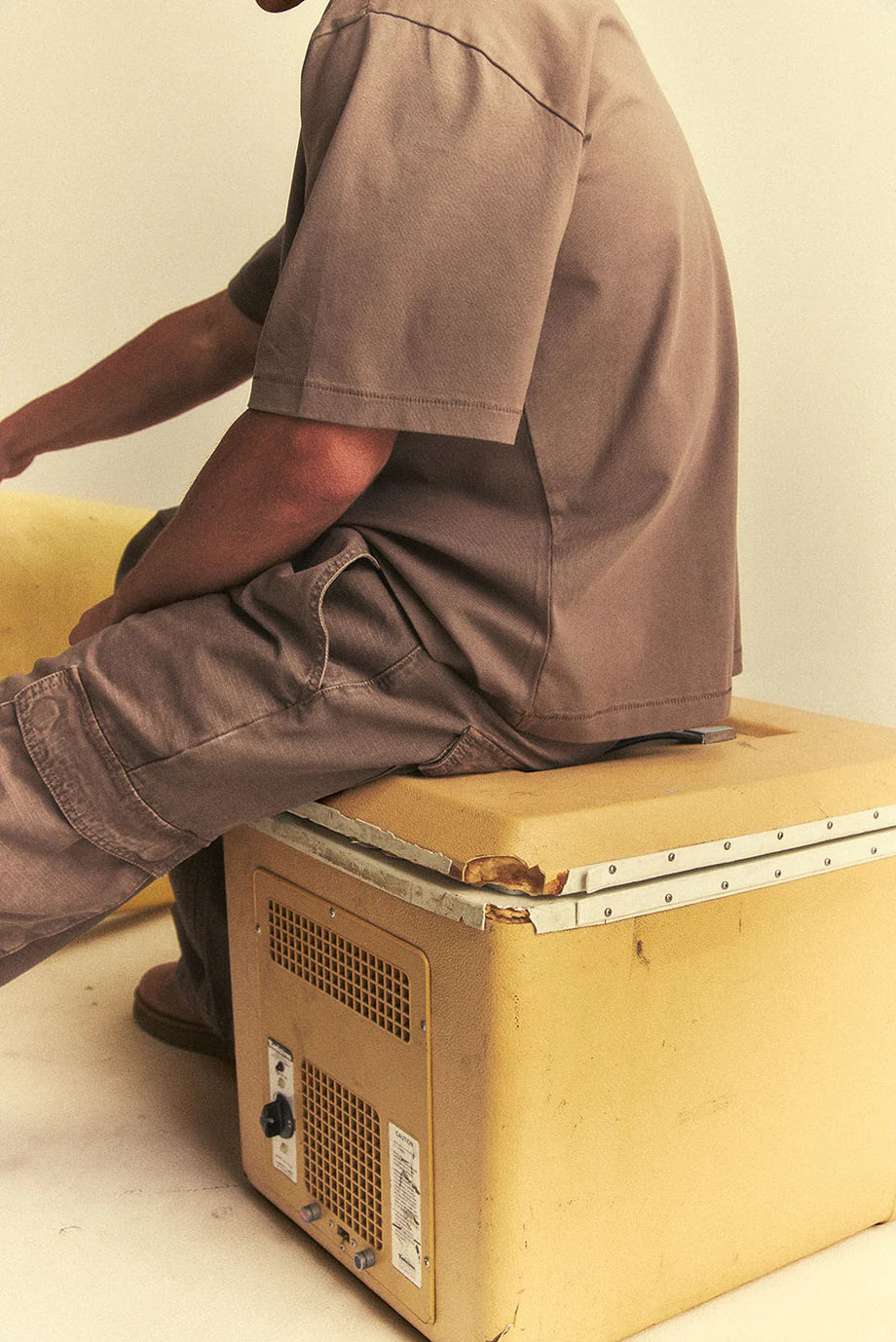 Person sitting on a wooden box with a metal frame, possibly on a white floor.