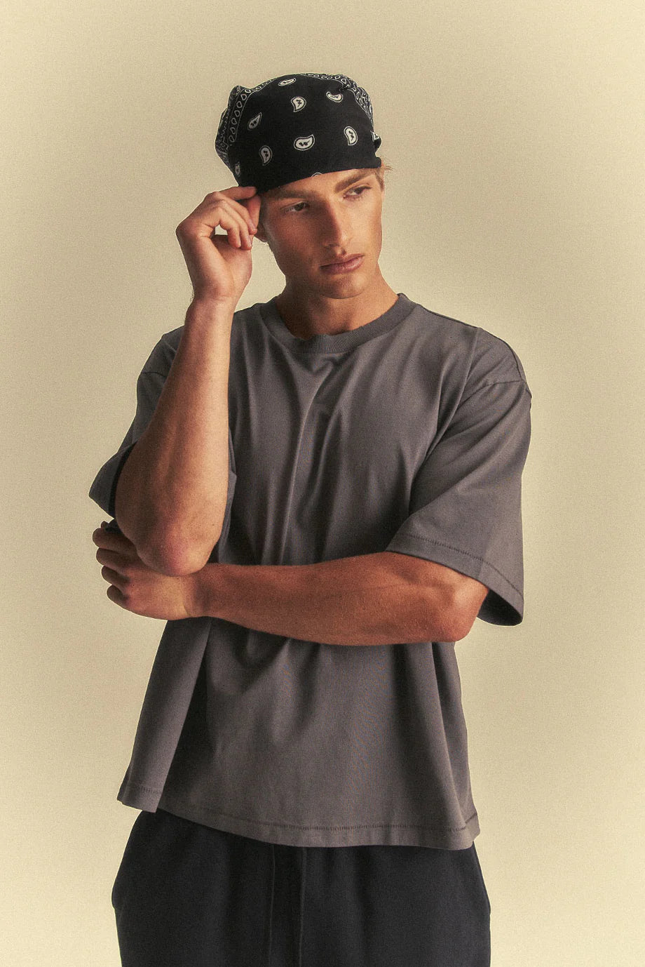 Man wearing a grey t-shirt and black bandana against a beige background