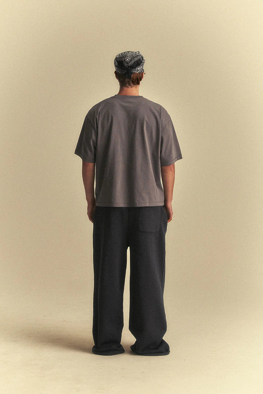 Person wearing a grey t-shirt and black pants standing against a beige background