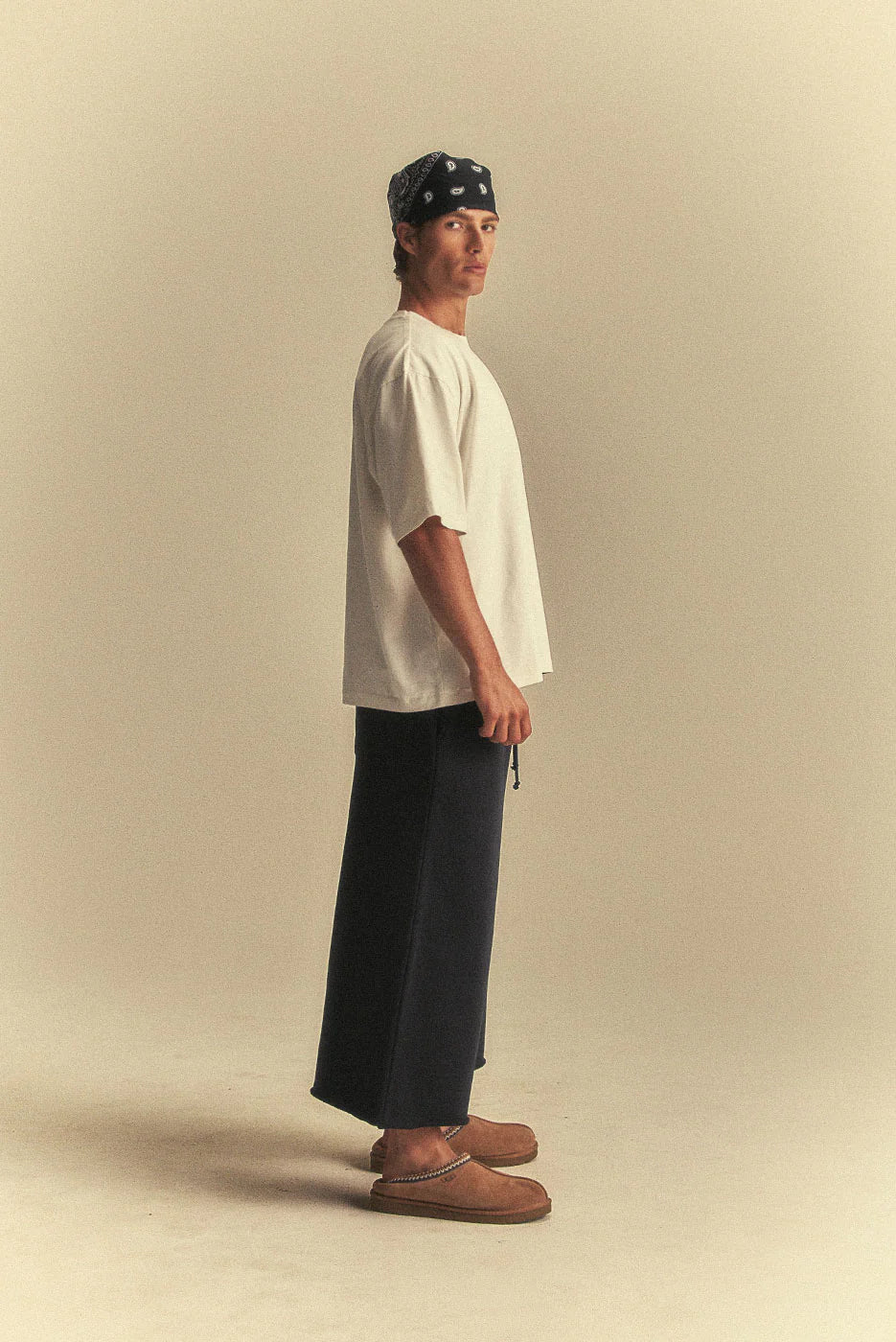 Person wearing a white t-shirt, dark pants, and a headband on a beige background