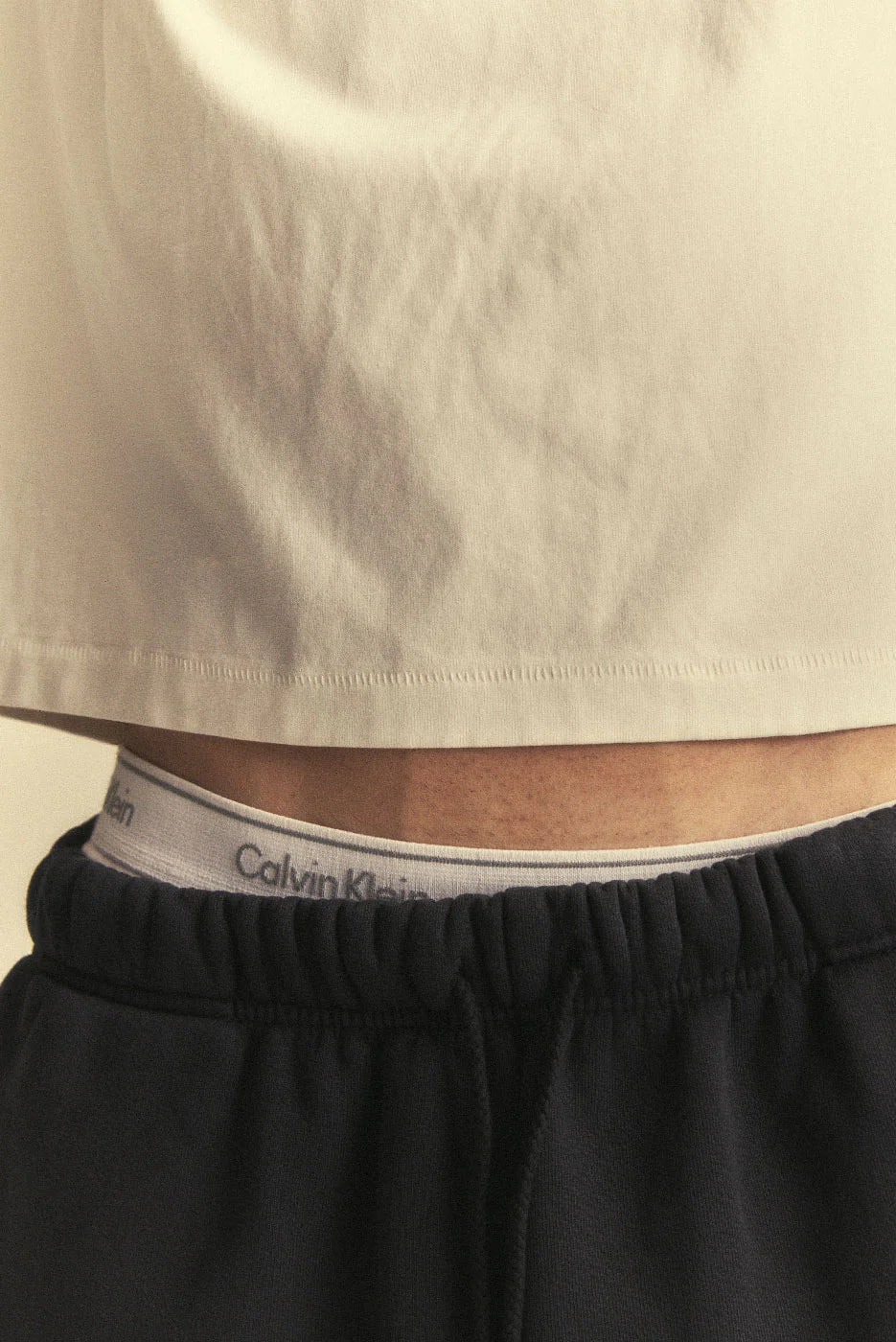 Close-up of a person wearing black shorts with a Calvin Klein logo on the waistband.