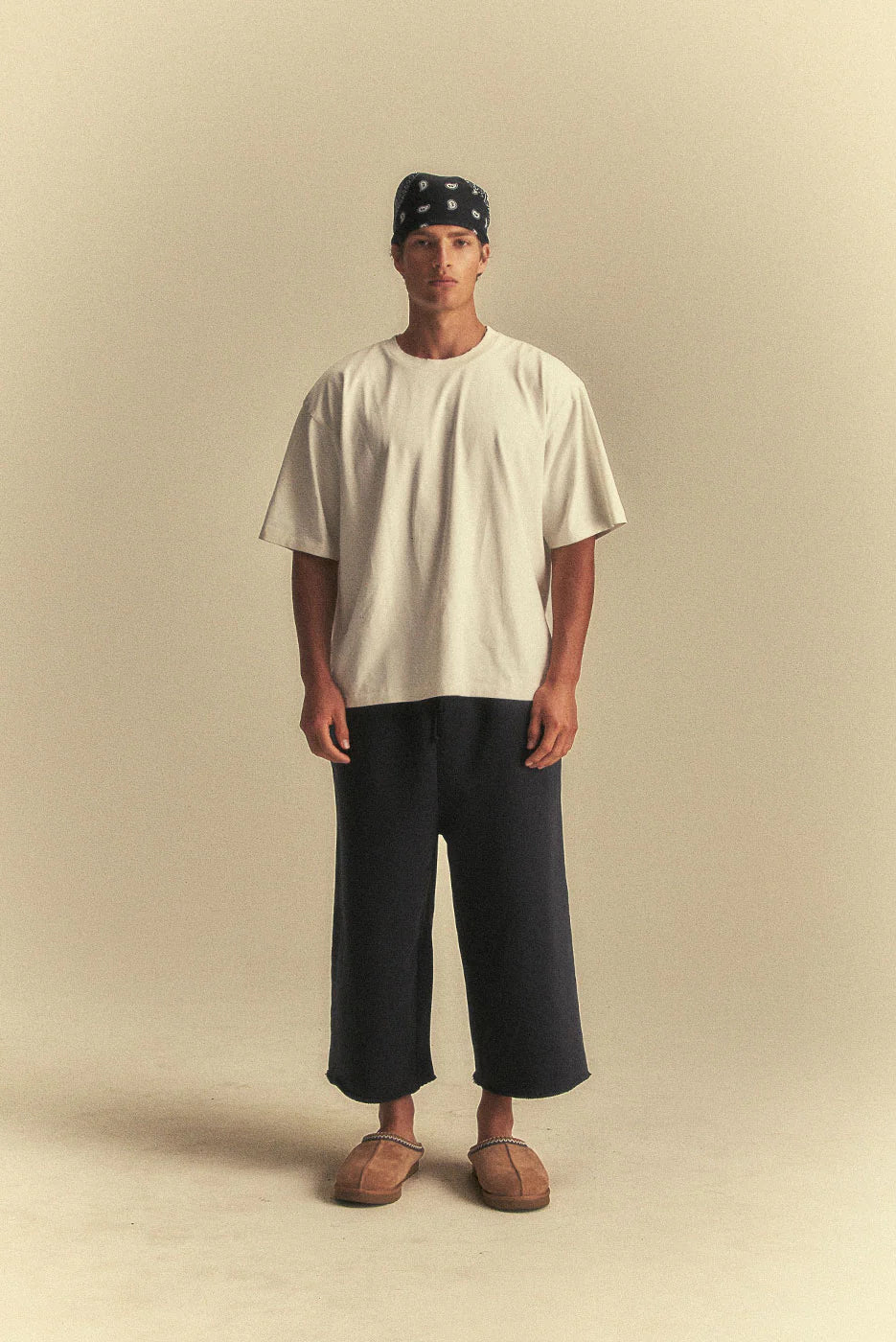 Person wearing a white t-shirt and dark pants on a beige background
