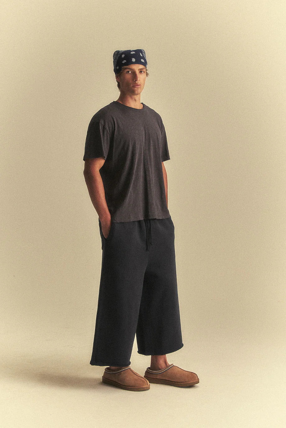 Person wearing a dark t-shirt, black wide-leg pants, and brown shoes on a beige background