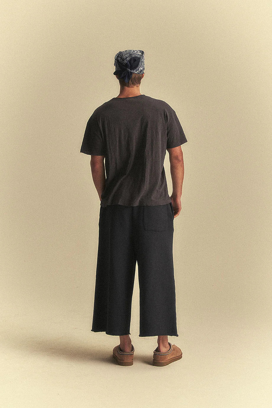 Person wearing a black t-shirt and wide-leg pants standing against a beige background