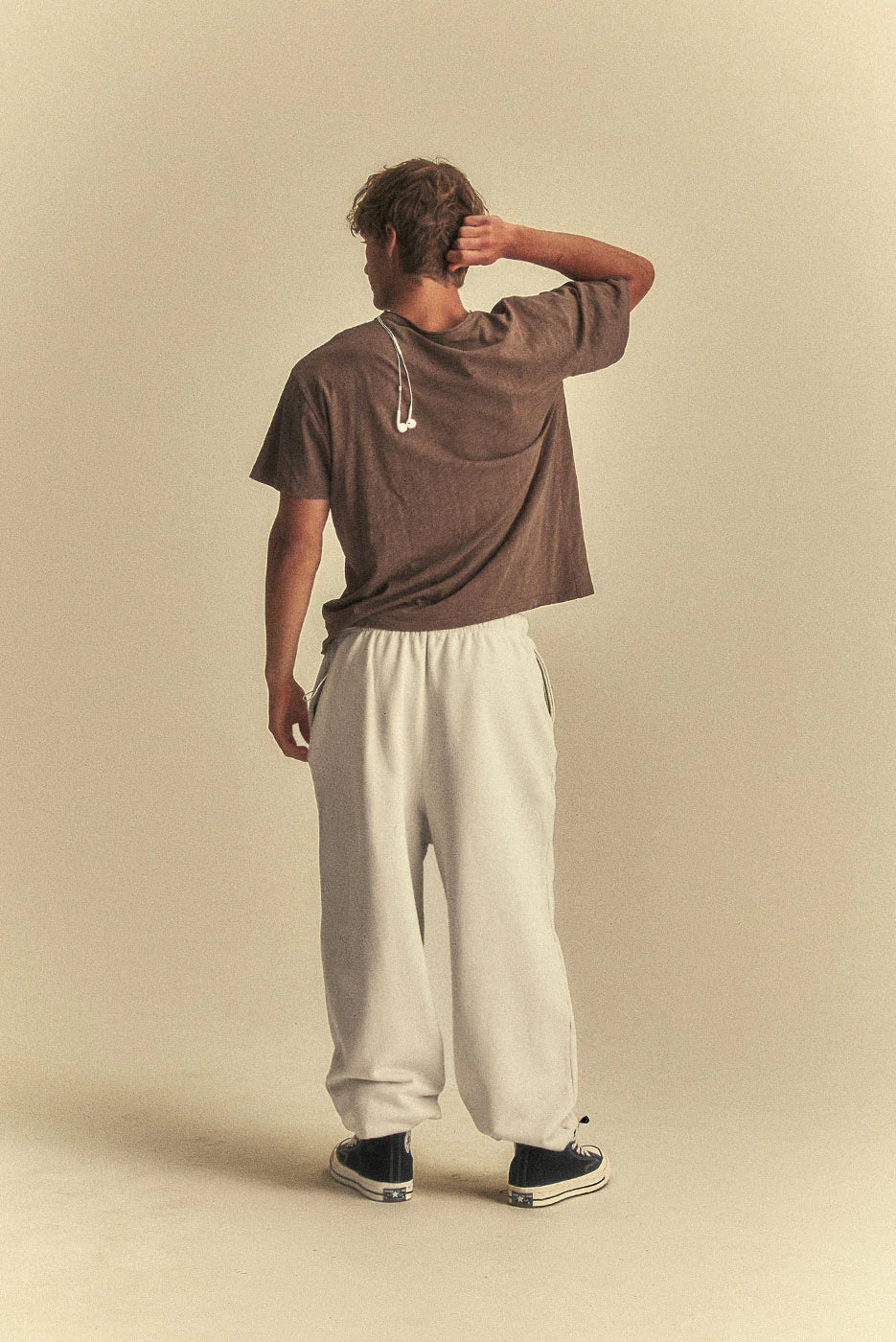 Person wearing a brown shirt and white pants against a beige background