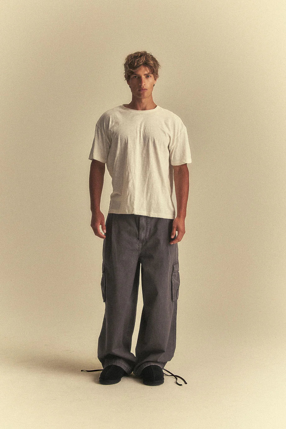 Man wearing a plain white t-shirt and grey cargo pants on a beige background