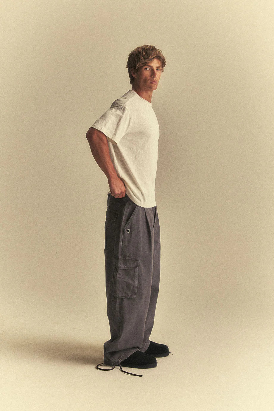 Man wearing a white t-shirt and grey cargo pants on a beige background
