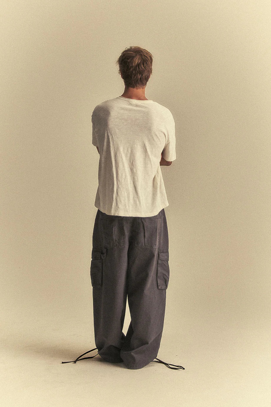 Person wearing a white shirt and dark pants on a beige background