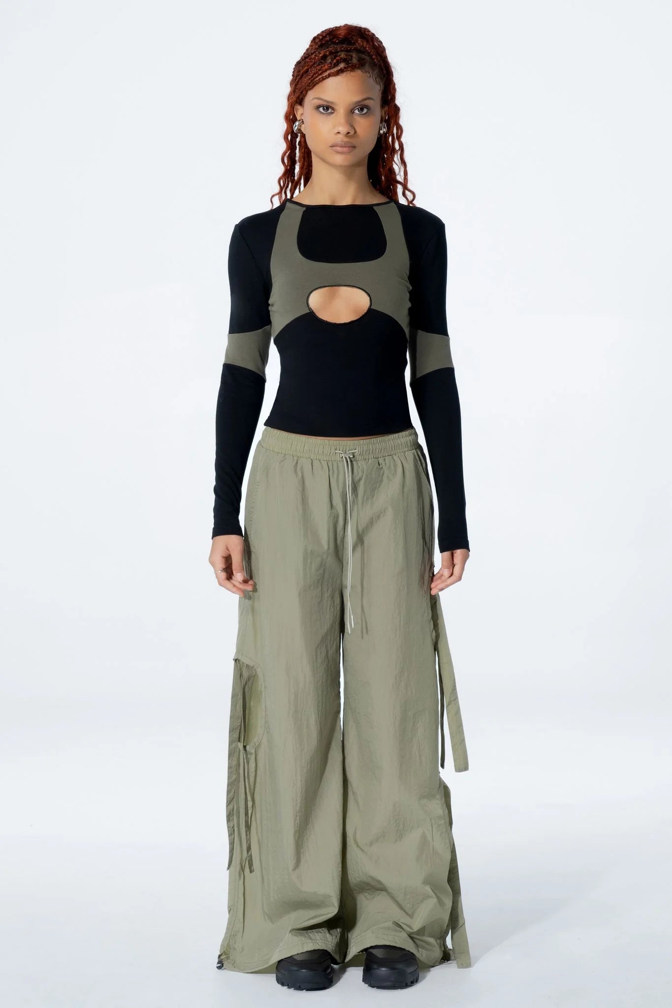 Woman wearing a black long-sleeve top with a cut-out design and pants on a white background