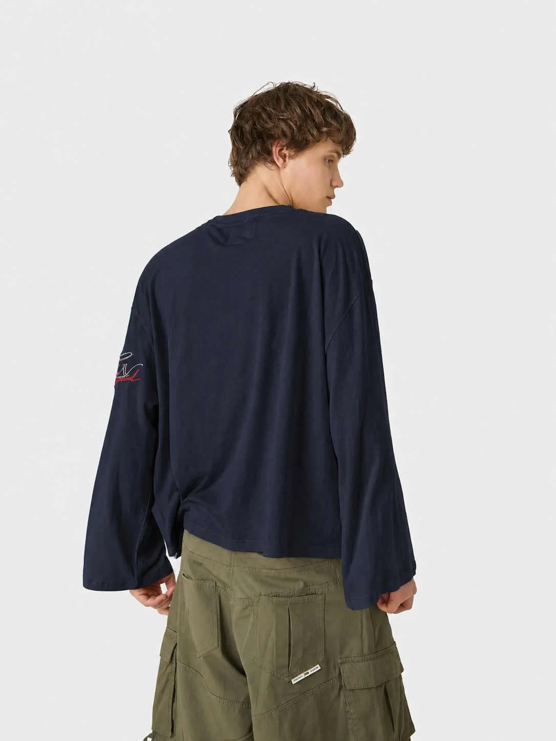 Person wearing a navy long-sleeve shirt with a patch on the back, standing against a white background