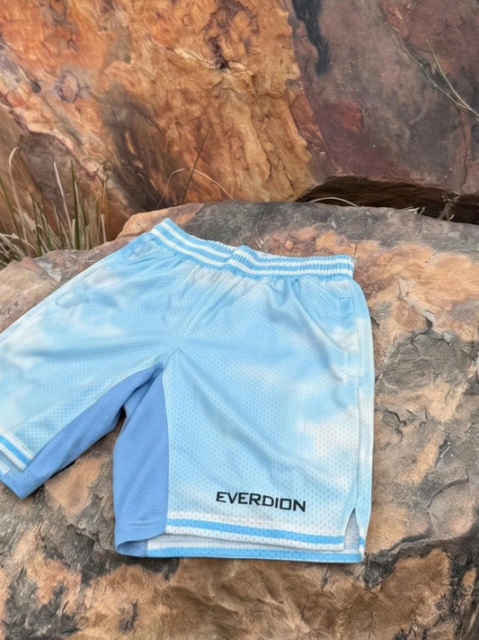 Light blue athletic shorts with a white tie-dye pattern, featuring the brand name 'EVERDION' printed in black near the hem, laid flat on a textured brown rock.
