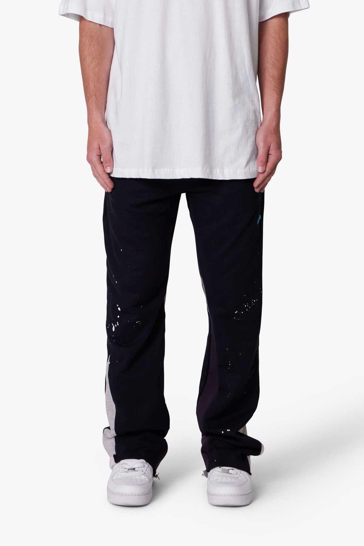 Person wearing black pants with white splashes and a white shirt on a white background
