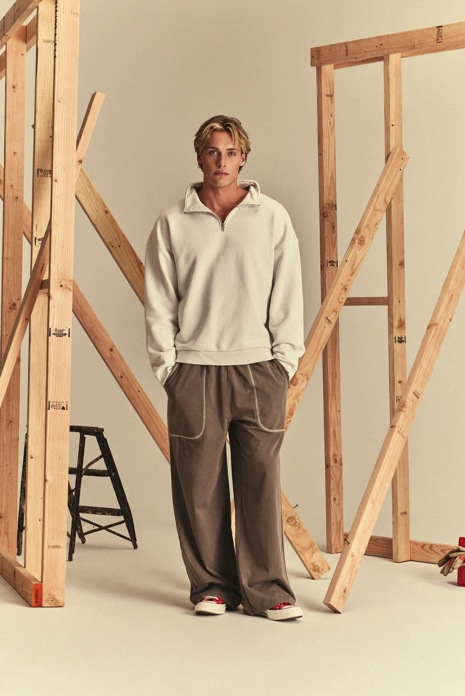 A model wearing a cream-colored half-zip pullover sweatshirt and brown wide-leg sweatpants.