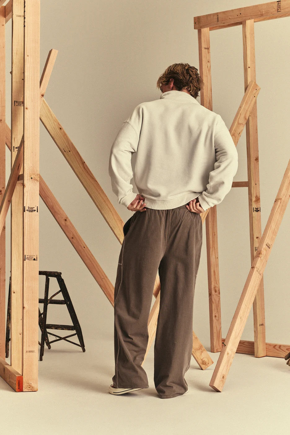 A model wearing a cream-colored half-zip pullover sweatshirt and brown wide-leg sweatpants.