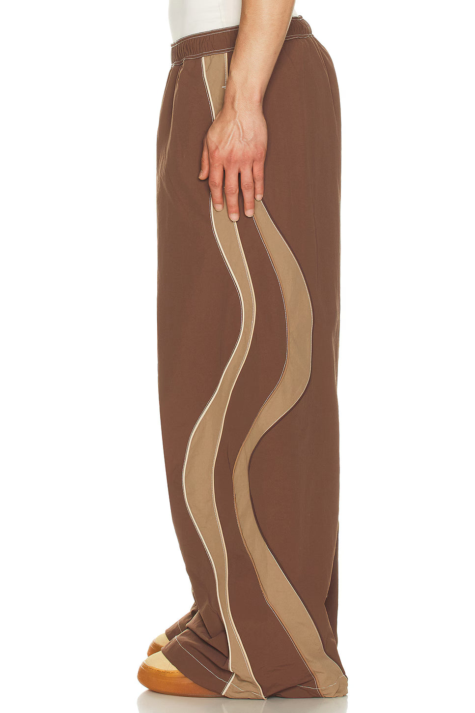 Brown pants with wavy beige pattern worn by a person on a white background