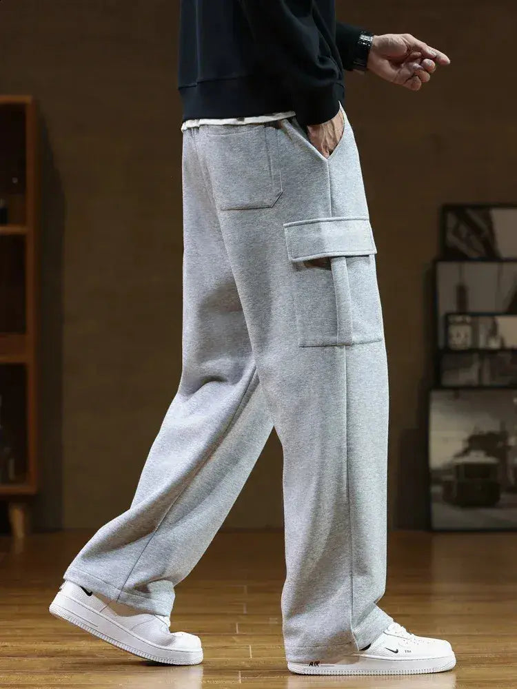 Person wearing grey cargo pants and white sneakers in a room with a wooden floor and a bookshelf.