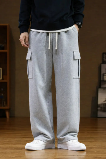 Person wearing grey cargo sweatpants and white sneakers in a room with wooden floor and bookshelf.