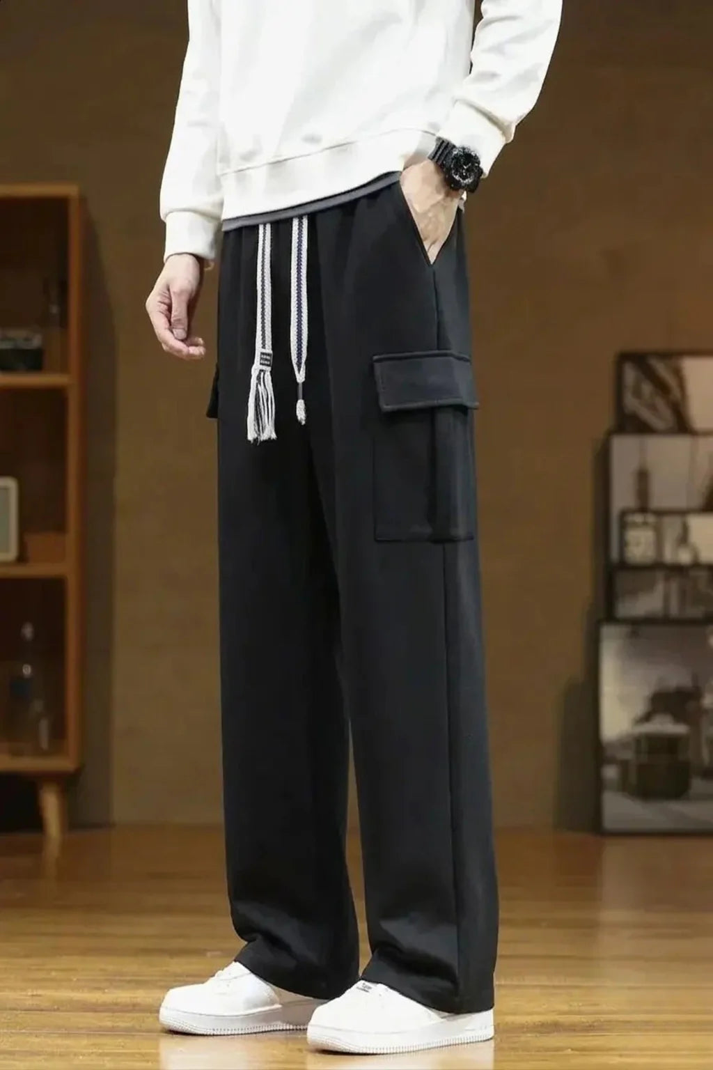 Person wearing black cargo sweatpants and white sneakers in a room with wooden floor and bookshelf.