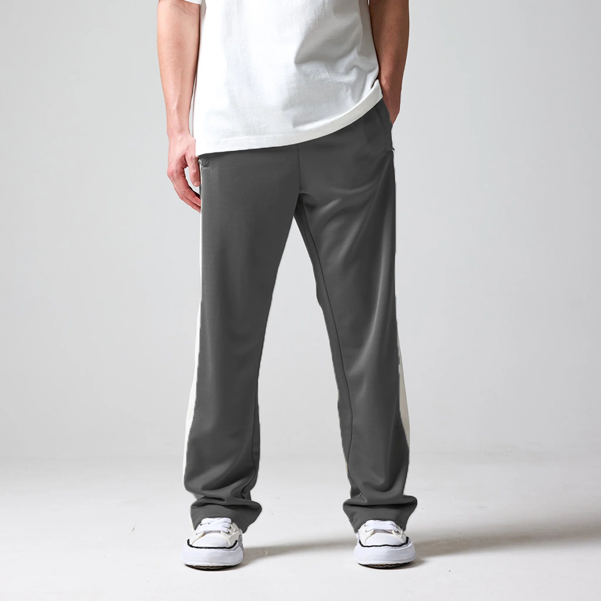 A person wearing grey pants and a white shirt on a plain background