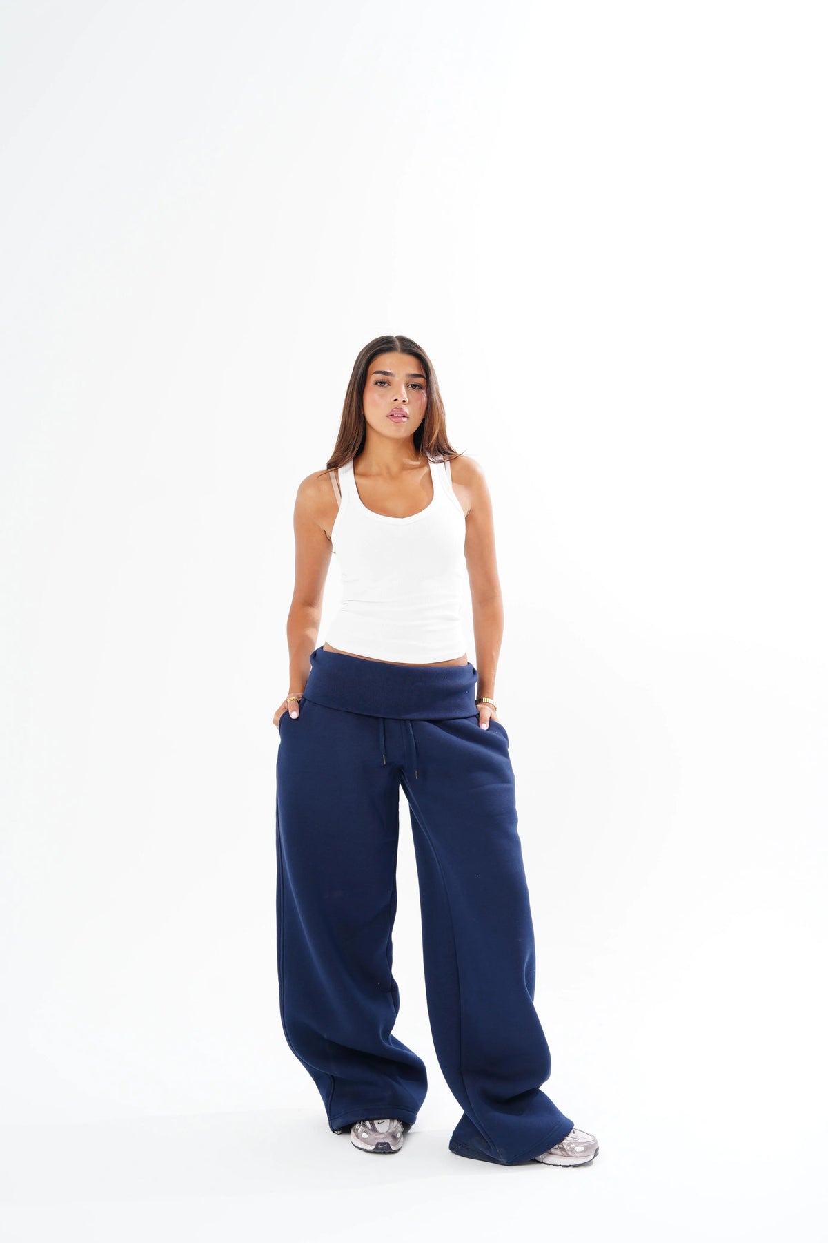 A woman modeling black wide-leg sweatpants and a white tank top against a solid white studio background.