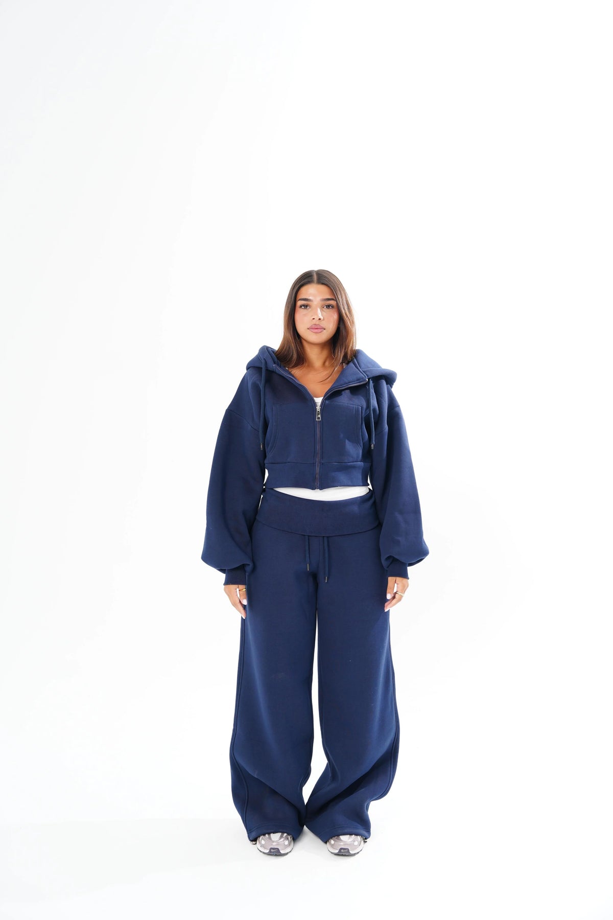 A model wearing a matching navy blue lounge set consisting of a cropped zip-up hoodie with a hood and wide-leg sweatpants.