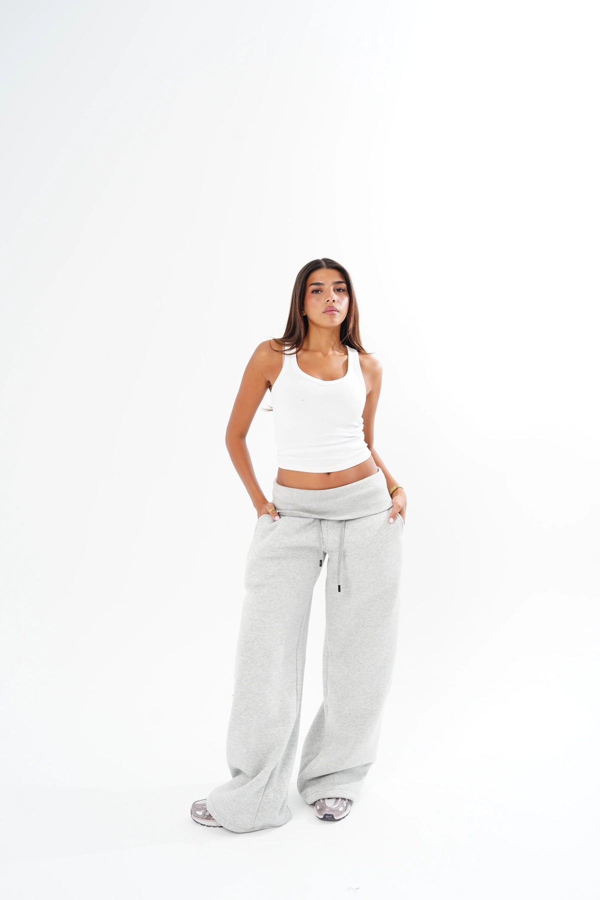 A woman modeling a white ribbed tank top and light grey wide-leg sweatpants against a seamless white studio background.