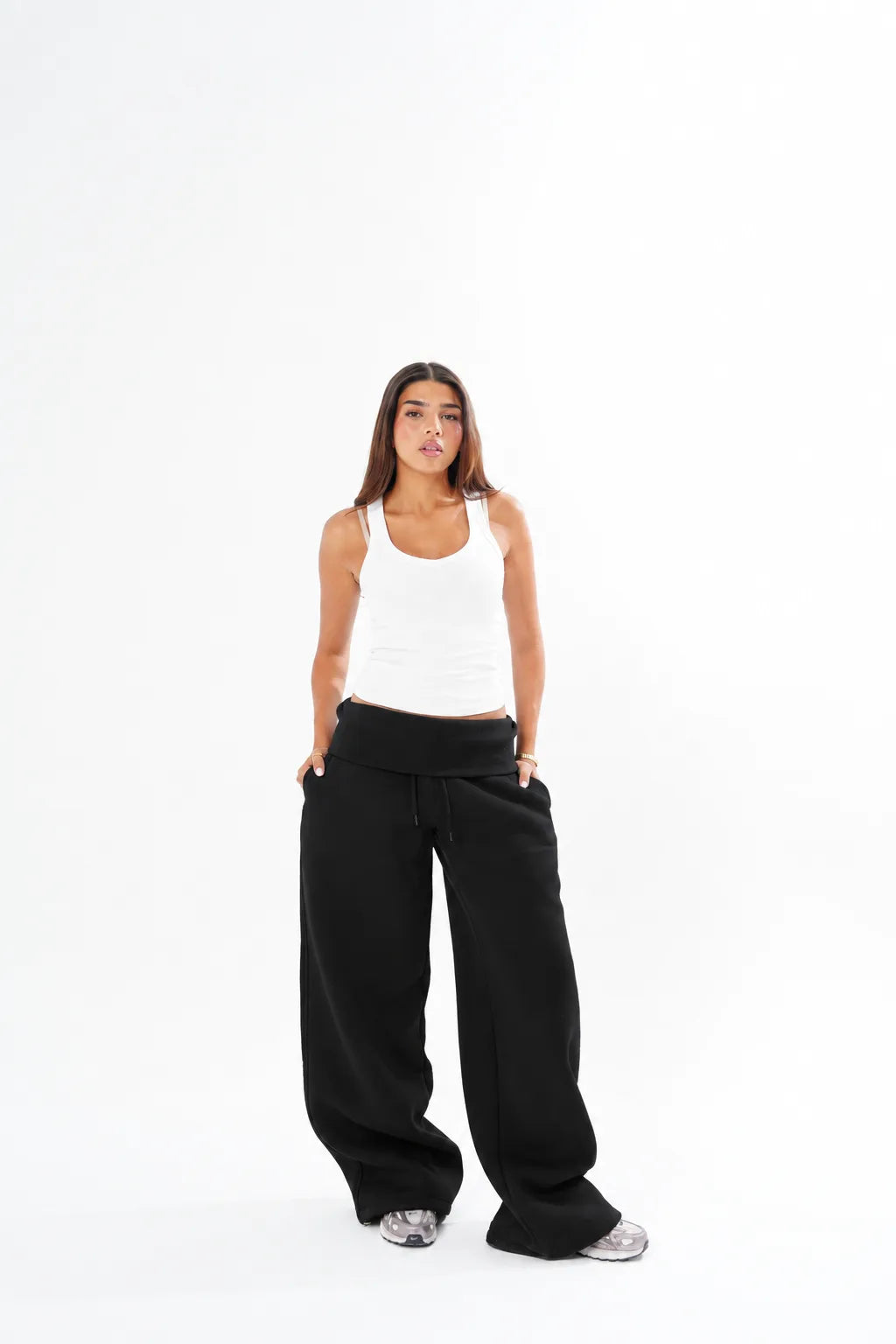 A woman modeling black wide-leg sweatpants and a white tank top against a solid white studio background.