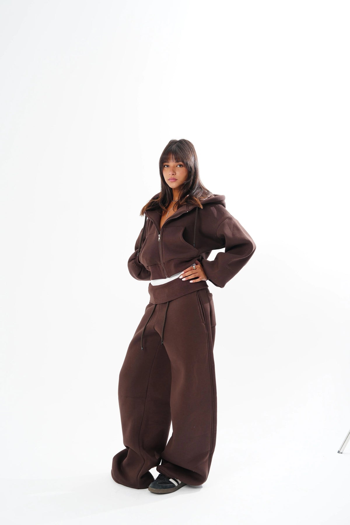 A model wearing a matching dark brown zip-up hoodie and wide-leg sweatpants set, standing against a plain white studio background.