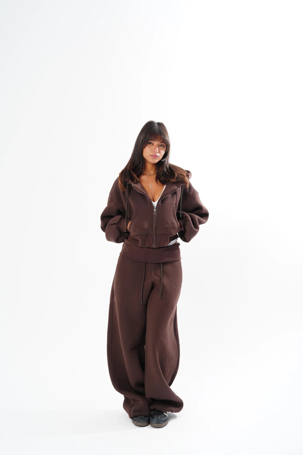 A woman modeling a matching dark brown zip-up hoodie and wide-leg sweatpants set against a plain white studio background.