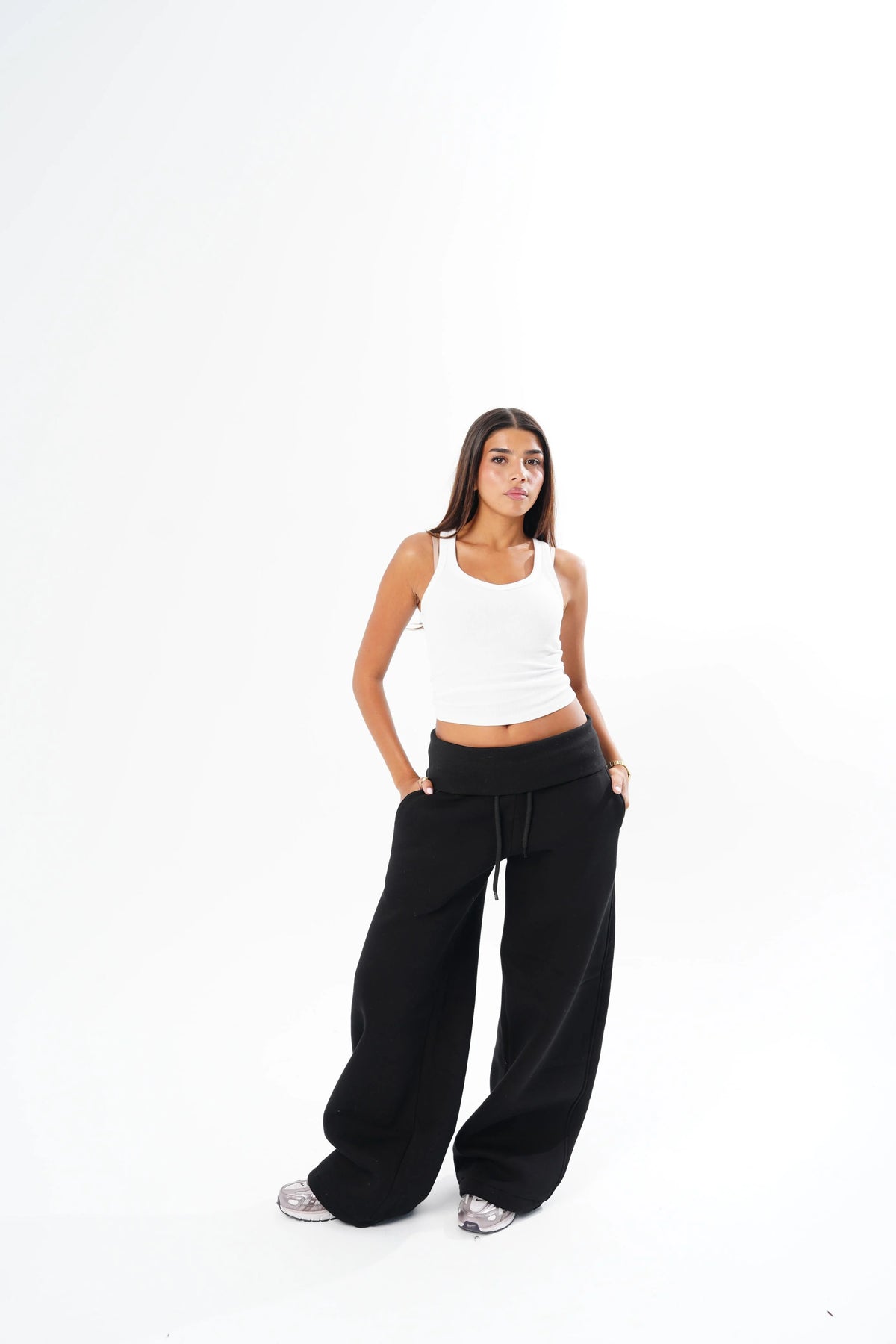 A woman modeling a white ribbed tank top and black wide-leg sweatpants against a seamless white studio background.