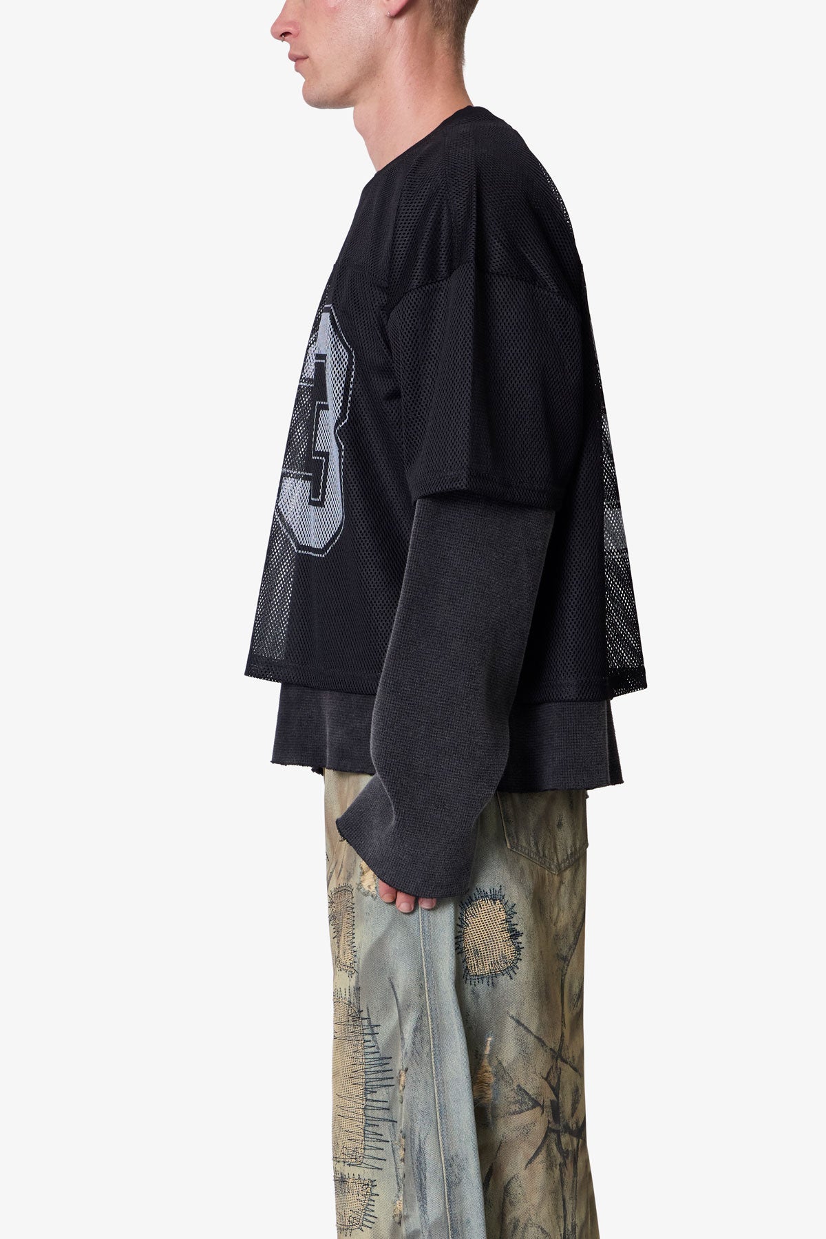 Person wearing a black oversized jersey with a logo, standing against a white background