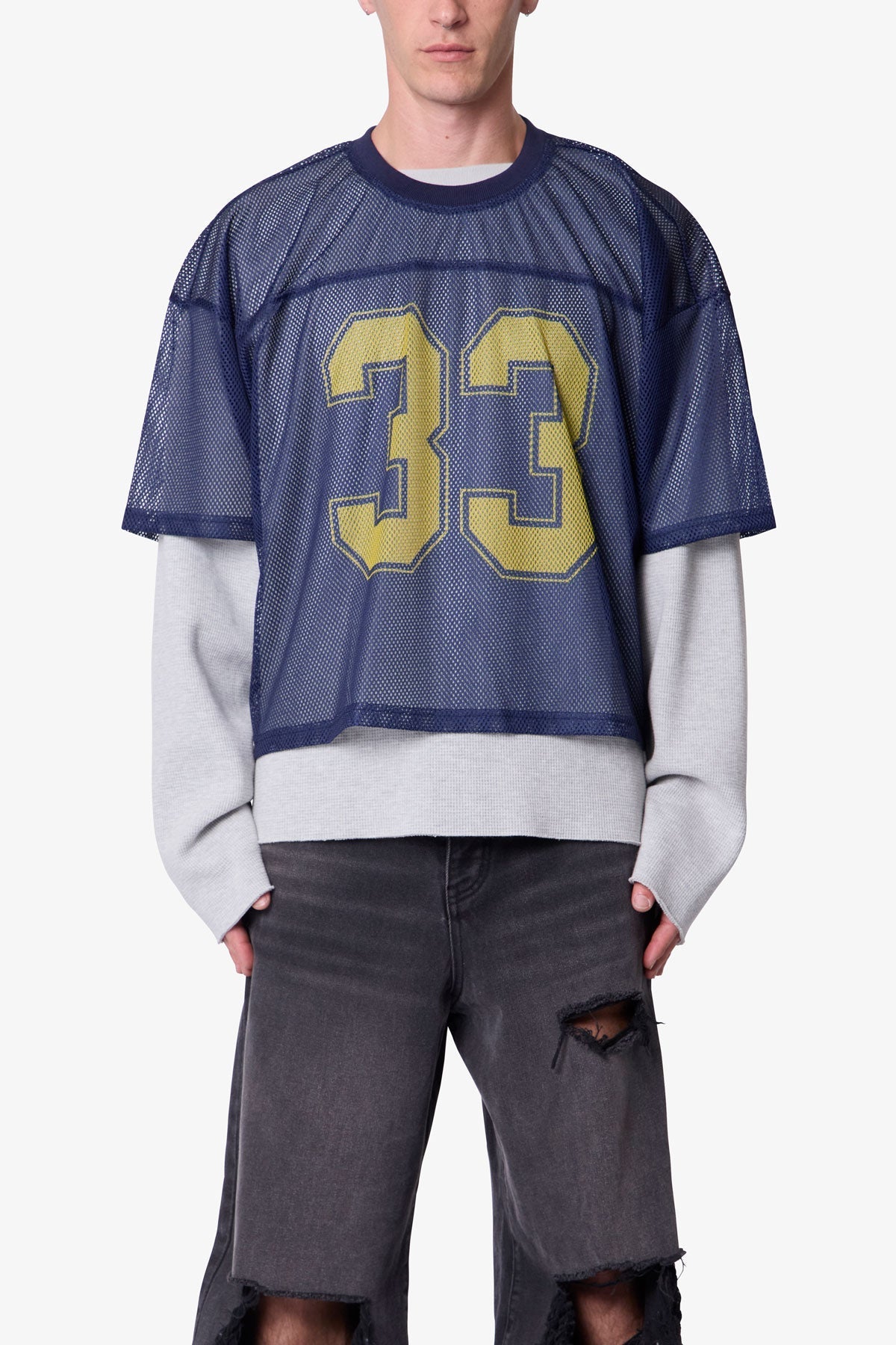 Person wearing a sheer navy jersey with yellow number 33 over a white shirt and grey pants on a white background