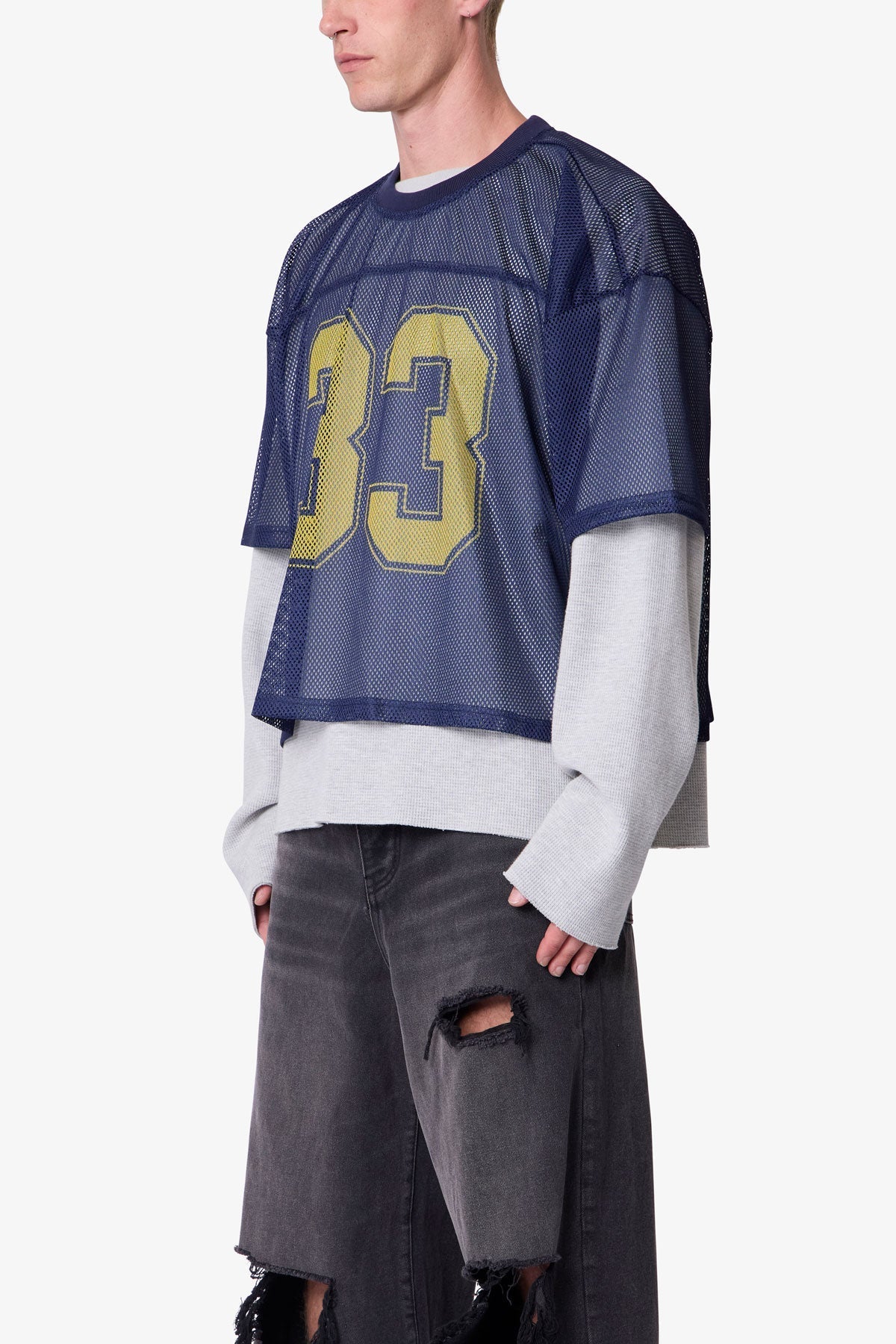 Person wearing a blue sports jersey with yellow number 33 and gry pants on a white background