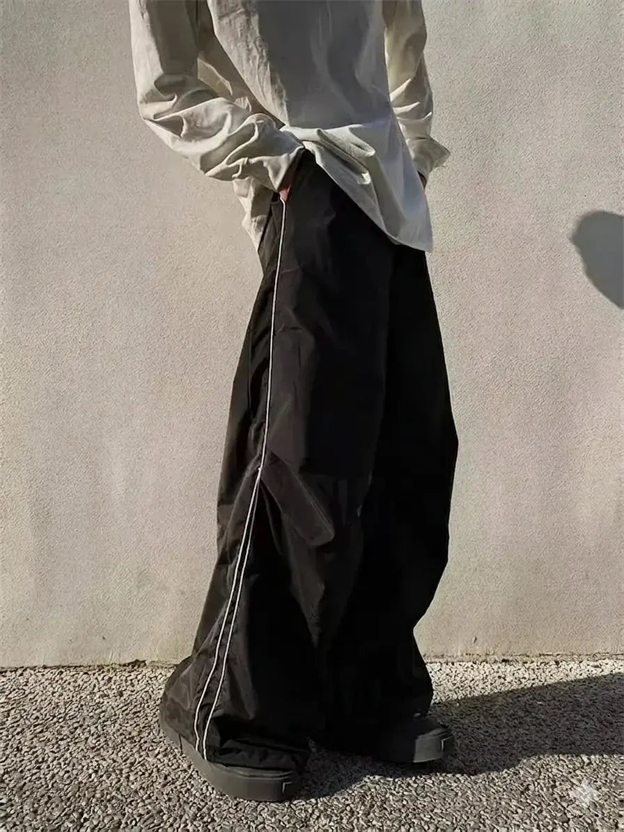 Person wearing a light-colored shirt and dark pants against a plain wall.