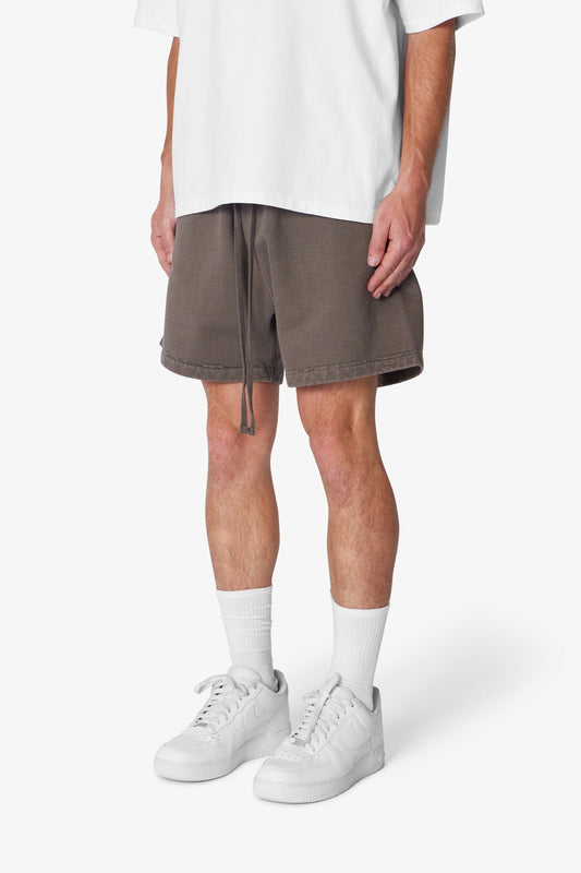 Person wearing brown shorts, white sneakers, and socks on a white background