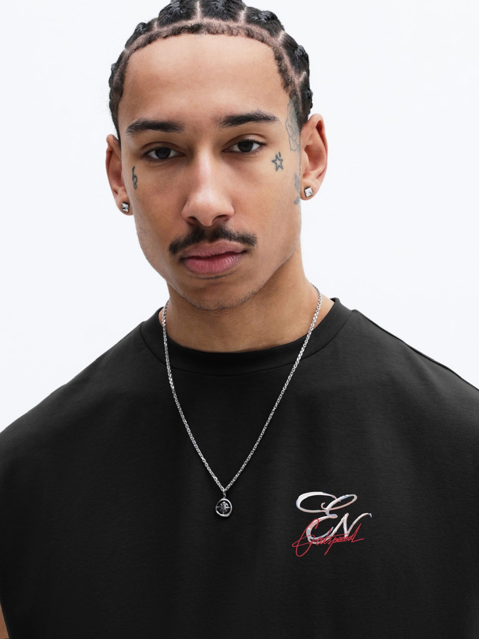 Man wearing a black shirt with a logo and a necklace on a white background
