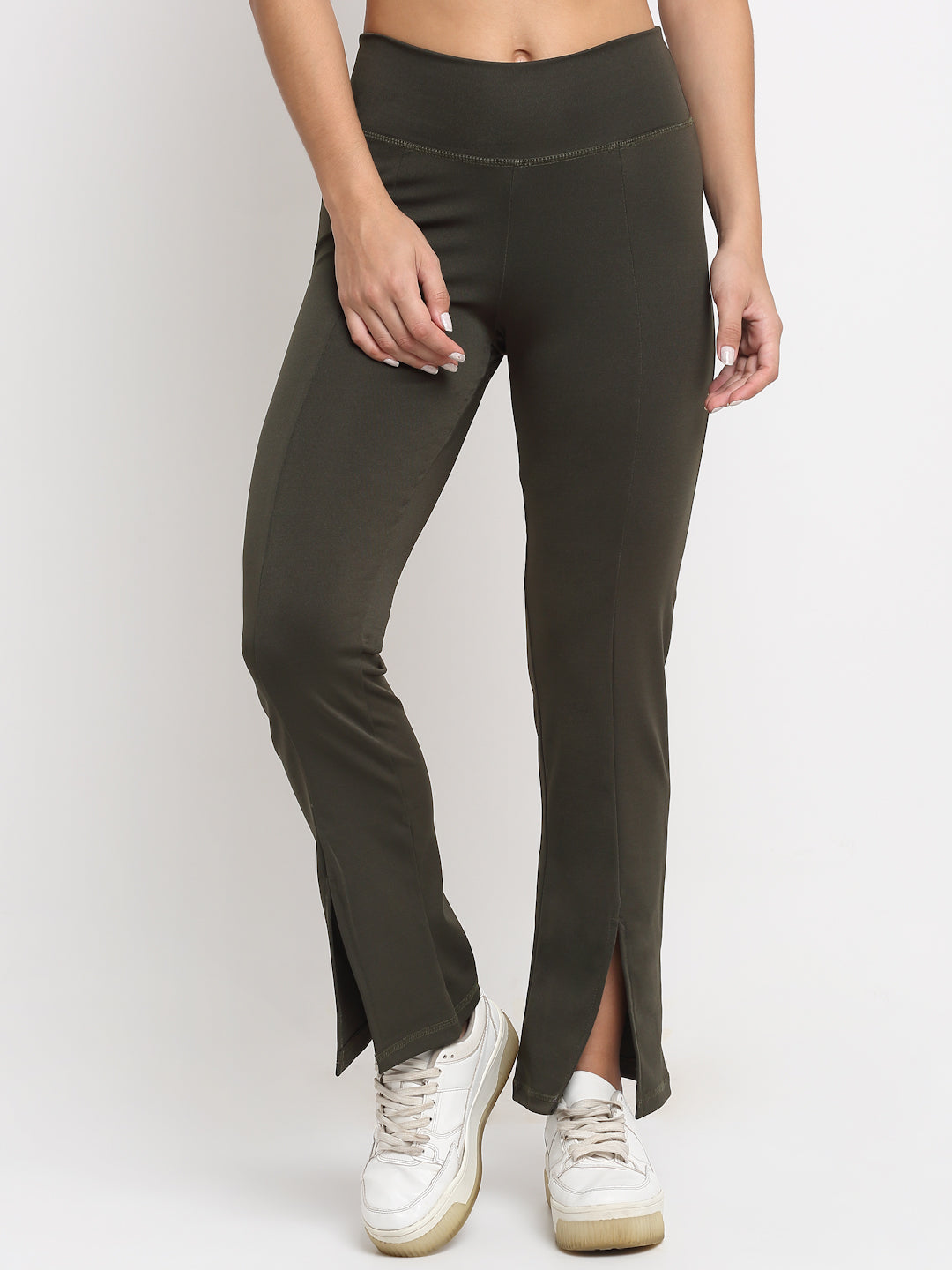 A pair of high waist green yoga pants with front slits and a flared leg design, being modeled by a person wearing white sneakers.
